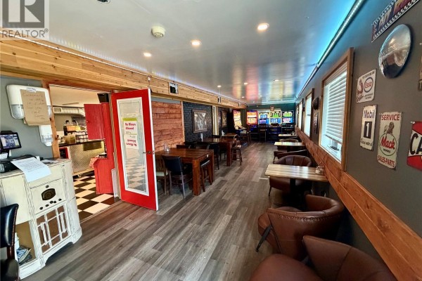 Interior view showing a dining area, kitchen entrance, and slot machines in the distance. - 1020 Railway Avenue, Carnduff