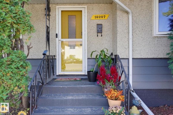 Close-up of the yellow front door with glass panes, house number 10207, and potted plants. - 10207 & 10209 120 Av Nw, Edmonton