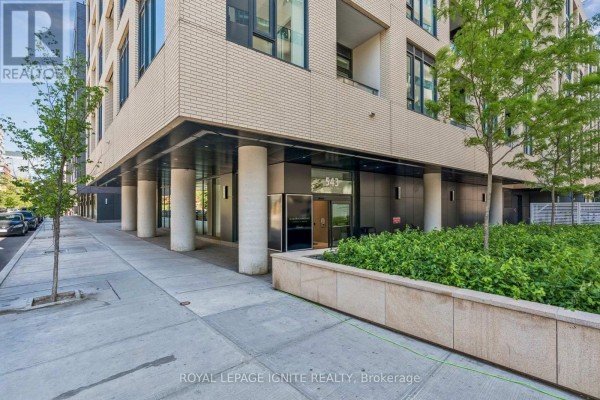 Sidewalk view of apartment building entrance with concrete pillars and surrounding greenery. - 1021 - 543 Richmond Street W, Toronto