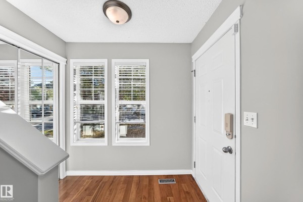 Interior entryway with light gray walls, wood floors, a white door, and two windows. - 1022 80 St Sw, Edmonton