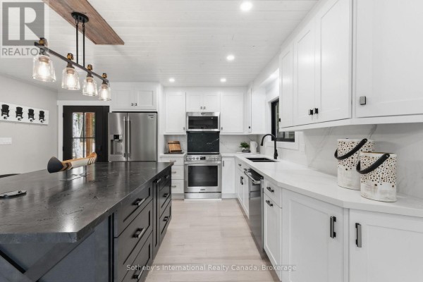 Modern kitchen with white cabinets, dark island, stainless steel appliances, and hardwood floors. - 1023 Strachan Point Road, Muskoka Lakes)