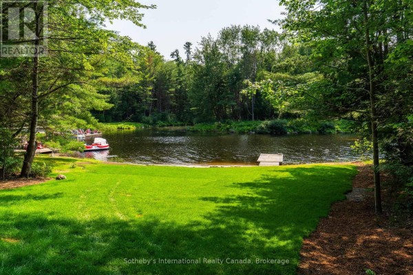 Lakeside view with green lawn, dock, red paddle boats, and trees surrounding the water. - 1023 Strachan Point Road, Muskoka Lakes)