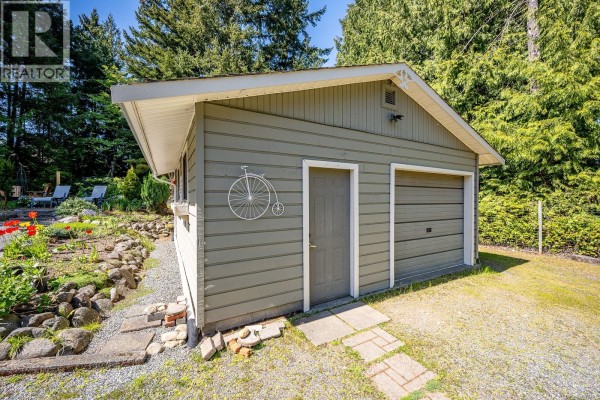 Backyard patio with a glass table and chairs, adjacent to a raised deck and green lawn. - 1023 Sylvan Rd, Comox