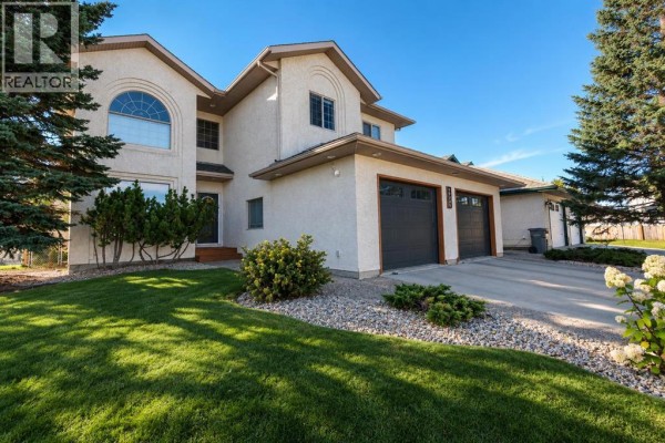 Side view of the house exterior, showing the stucco finish, arched window, and manicured lawn. - 10235 75a Avenue, Grande Prairie