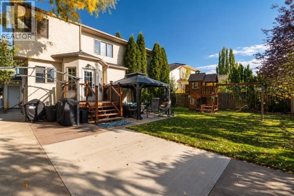 Backyard view with a wooden deck, gazebo, play structure, and lawn surrounded by trees and fencing. - 10235 75a Avenue, Grande Prairie