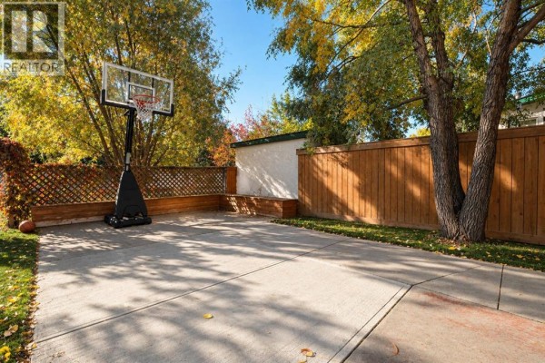 Concrete basketball court in the backyard with a wooden fence, tree, and green grass surrounding it. - 10235 75a Avenue, Grande Prairie