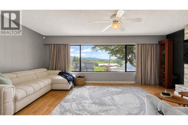 Living room with a large sectional sofa, grey rug, and a view of surrounding houses and trees. - 1024 Ranch Park Way, Coquitlam
