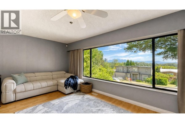 Living room with a sectional sofa and a wide view of suburban houses and distant mountains. - 1024 Ranch Park Way, Coquitlam