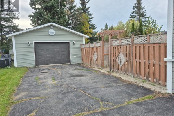 Exterior view of a detached garage with a dark brown door and wooden fence. - 1024 Rue Misho, Beresford
