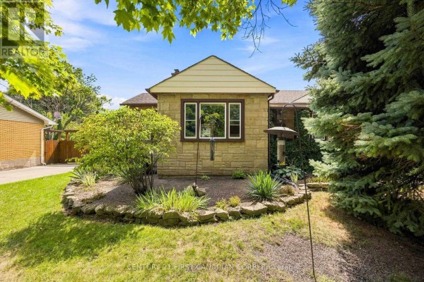Rear view of the stone house with a bird feeder and surrounding greenery. - 1027 London Road, Sarnia