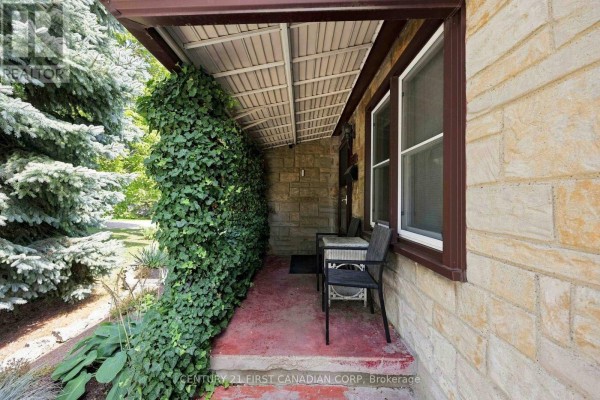 Close-up of the covered porch with a red floor, stone walls, and seating area. - 1027 London Road, Sarnia