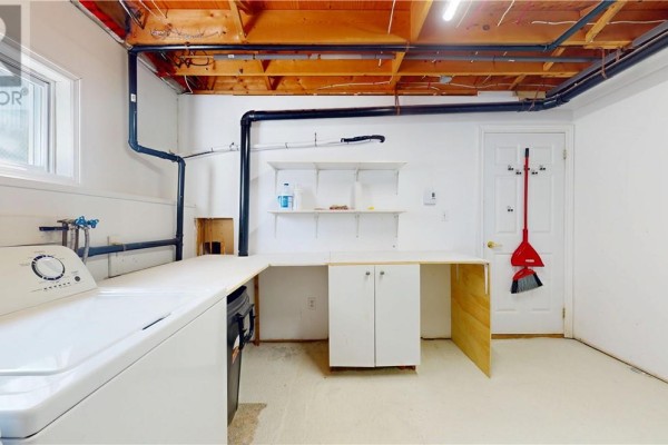 Basement laundry area with washing machine, utility sink, and unfinished ceiling. - 1028 Bay Estates, Nemi