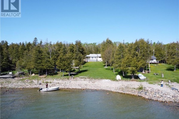Waterfront property with several homes nestled among trees, featuring a gravel shoreline. - 1028 Bay Estates, Nemi