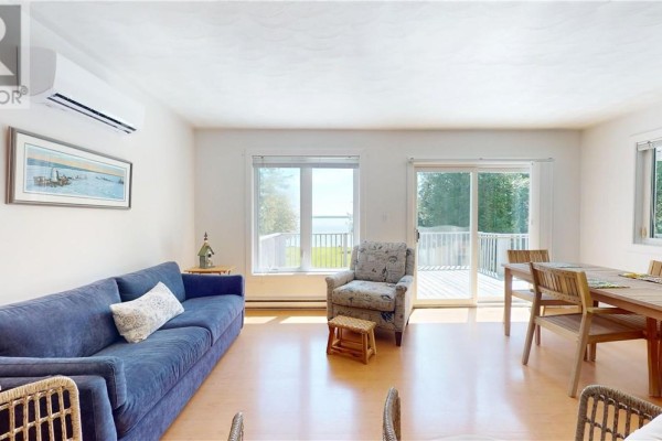 Living and dining area with sofa, chairs, dining table, and large windows overlooking water. - 1028 Bay Estates, Nemi
