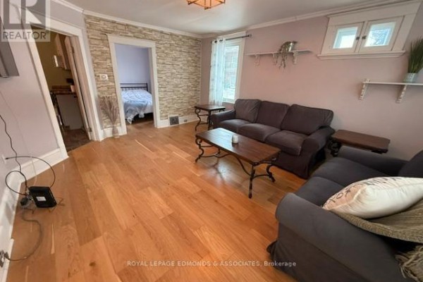 Living room with stone accent wall, hardwood flooring, and view into the bedroom. - 1028 Pembroke Street E, Pembroke