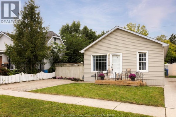 Exterior side view of a beige vinyl-sided bungalow with neighboring houses and trees. - 1028 Reedmere Rd, Windsor