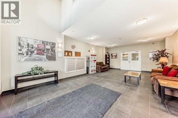 Carpeted bedroom with neutral walls and doorway leading to kitchen area. - 103, 10 Auburn Bay Link Se, Calgary