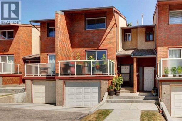 A fenced backyard patio with wicker furniture, a coffee table, and various plants. - 103, 1305 Glenmore Trail Sw, Calgary