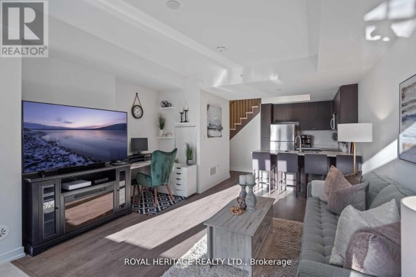 Living space with television, desk, and connected kitchen with island and bar stools. - 103 - 1555 Kingston Road, Pickering