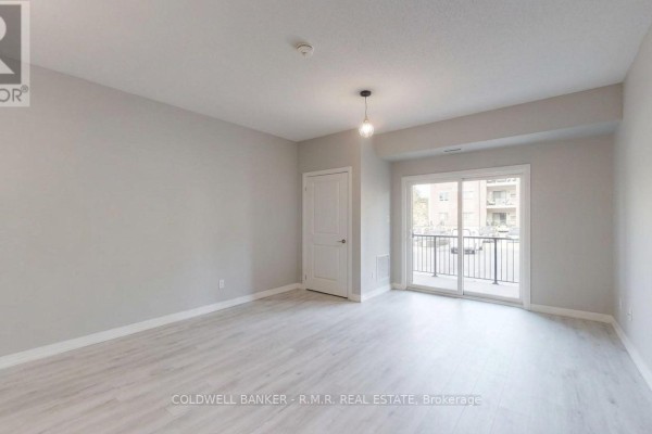 Living area with light grey walls, white door, sliding balcony door, and light wood flooring. - 103 - 157 Wellington Street E, New Tecumseth