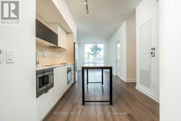 A galley kitchen with white cabinetry and stainless steel appliances and an adjacent dining area. - 103 - 20 Thomas Riley Road, Toronto