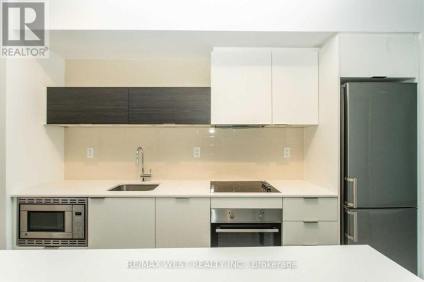 A close-up of a modern kitchen with white and dark wood cabinetry and a stainless steel refrigerator. - 103 - 20 Thomas Riley Road, Toronto