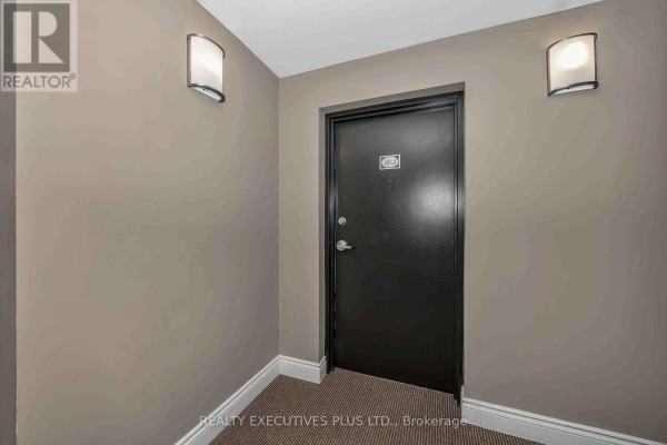 Hallway in an apartment building with a black door, two wall sconces, and beige walls. - 103 - 2376 Albert Street, Clarence Rockland