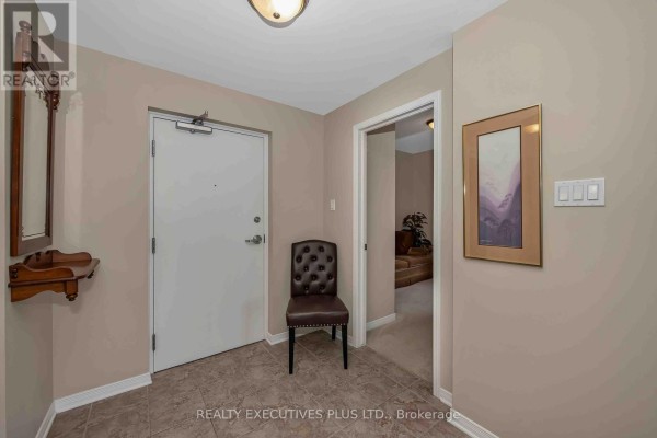 Apartment entrance with a white door, tufted chair, decorative shelf, framed artwork, and tiled floor. - 103 - 2376 Albert Street, Clarence Rockland