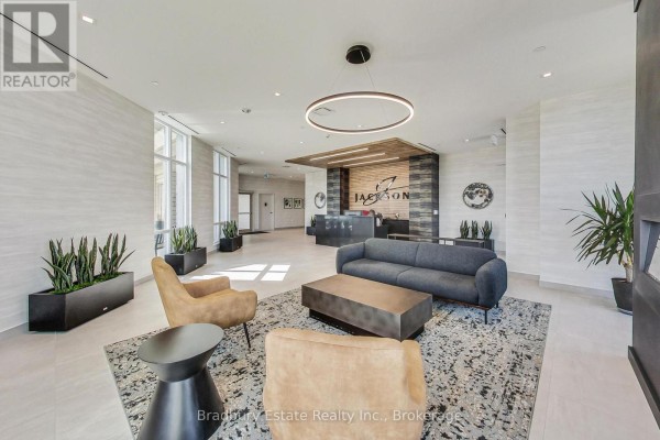 Apartment building lobby with modern furniture, plants, and a reception desk with the building name 'Jackson'. - 103 - 2750 King Street E, Hamilton
