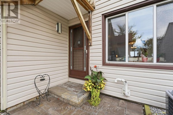 Exterior view of a townhouse entrance with beige siding and a brick patio. - 103 - 43 Olive Crescent E, Orillia