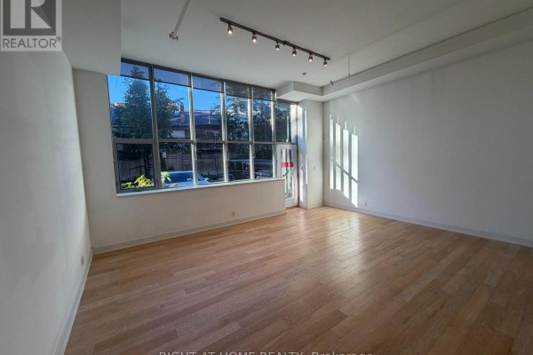 Empty spacious room with hardwood floors and large windows showing tree reflections. - 103 - 510 King Street E, Toronto