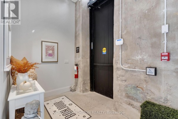 Interior hallway with concrete walls, a black door, fire extinguisher, and decorative entryway table. - 103 - 58 Grand Avenue, Cambridge