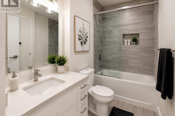 Bathroom with white vanity, toilet, bathtub with glass enclosure, and gray tiled walls. - 103 - 690 King Street W, Kitchener