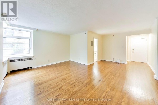 Empty living room with light beige walls, hardwood floors, and large windows. - 103 - 717 Eglinton Avenue W, Toronto