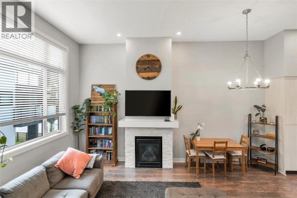 Living room features a large sectional sofa, electric fireplace with stone surround, and TV. - 103 1202 Nova Crt, Langford