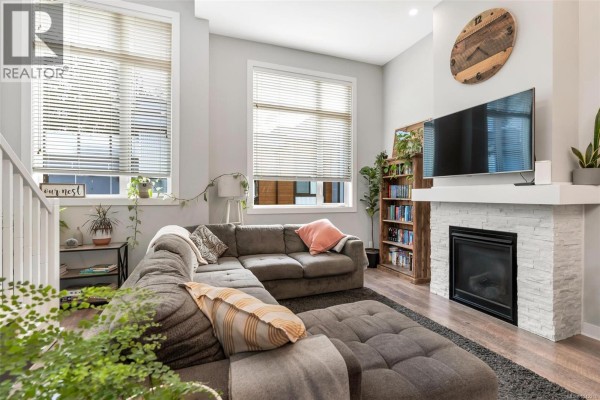 Living room with fireplace, television, large sectional sofa, and windows with blinds. - 103 1202 Nova Crt, Langford