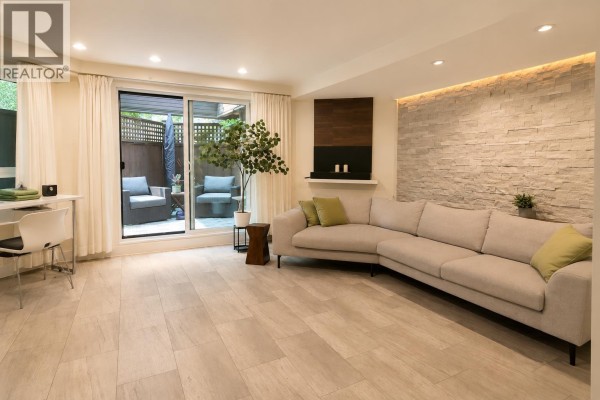 Living room with sectional sofa, stone accent wall, and sliding door to patio. - 103 1855 Nelson Street, Vancouver