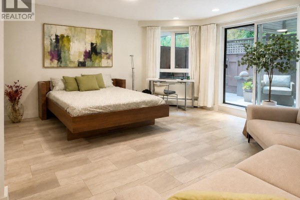 Bedroom with a wooden platform bed, abstract art, and patio access. - 103 1855 Nelson Street, Vancouver