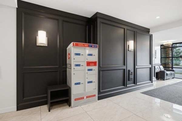 Building lobby detail with parcel lockers, dark wood paneling, and wall sconces. - 103 2860 Trethewey Street, Abbotsford