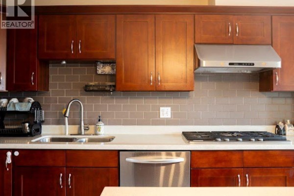 Kitchen view showing dark wood cabinets, stainless steel range hood, and subway tile backsplash. - 103 2880 Panorama Drive, Coquitlam