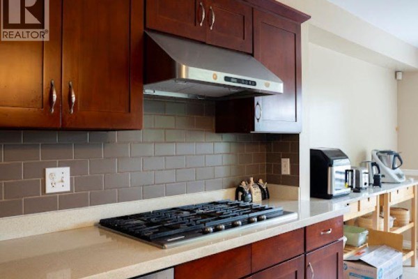 Close-up of a gas stovetop with a stainless steel range hood and dark wood cabinetry. - 103 2880 Panorama Drive, Coquitlam