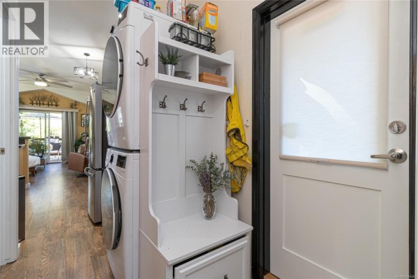 Interior view of a laundry area with stacked washer and dryer and white storage bench. - 103 3042 River Rd, Chemainus