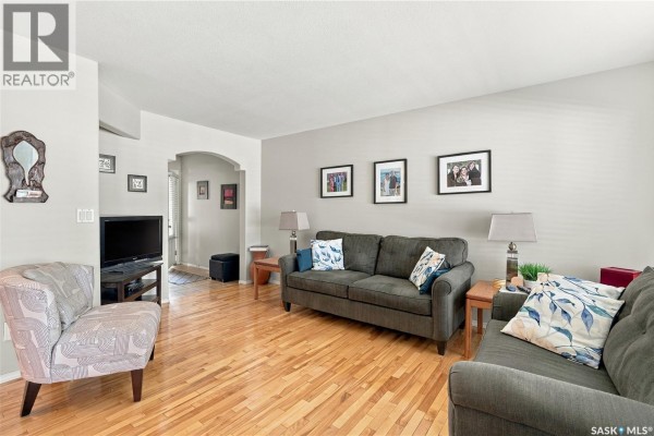 Living room with hardwood floors, grey sofa, armchair, and accent chair. - 103 445 Bayfield Crescent, Saskatoon