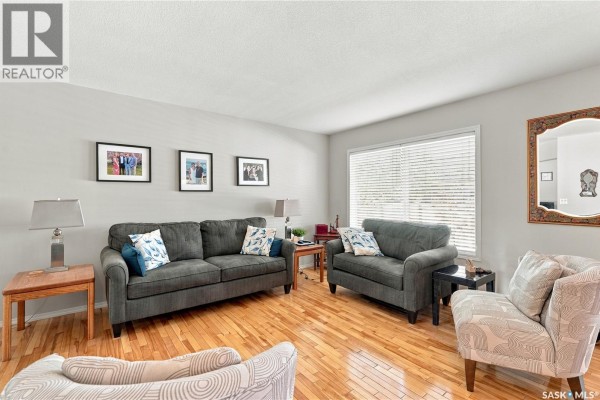 Living room with hardwood floors, sofa, loveseat, accent chair, and large window. - 103 445 Bayfield Crescent, Saskatoon