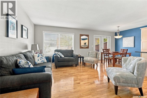 Living and dining area with hardwood floors, sofas, dining table, and patio doors. - 103 445 Bayfield Crescent, Saskatoon