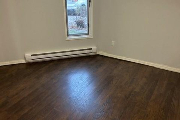 Corner of a room with dark wood laminate flooring and a white baseboard heater. - 103 507 Tait Crescent, Saskatoon