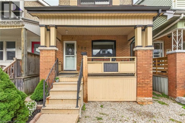 Close-up of the covered front porch with brick pillars and a wooden railing. Two chairs are visible on the porch. - 103 Belmont Avenue, Hamilton