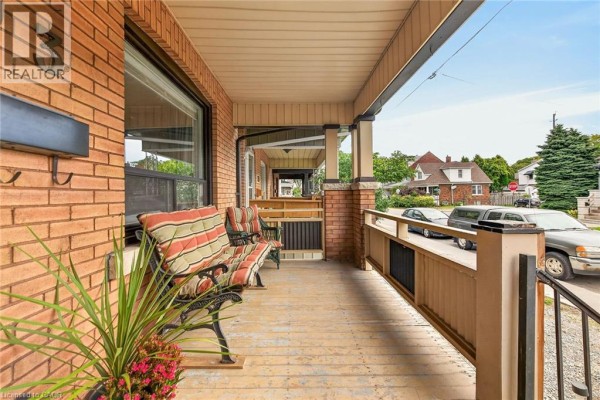 View from the front porch looking down the street. The porch has wooden floorboards and a railing, with seating. - 103 Belmont Avenue, Hamilton