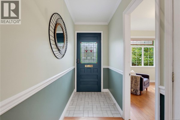 Interior view of a hallway with light green and grey walls, a dark blue front door with stained glass, and a tiled floor. - 103 Bushby St, Victoria