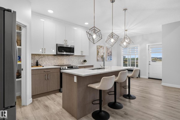 Modern kitchen with a large island, white quartz countertops, and stainless steel appliances. - 103 Edgefield Wy, St  Albert
